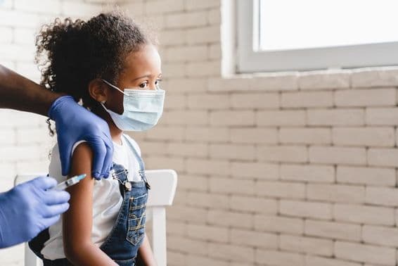 Girl receiving a vaccine with a mask on her face.