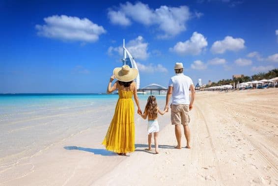 Young family with a daughter walking on the beach, Burj Al Arab in the background.