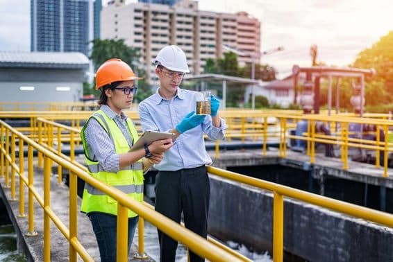 Two people in helmets inspecting water quality at a sewage treatment plant.