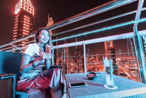 Young woman sipping cocktail on Dubai rooftop bar terrace.