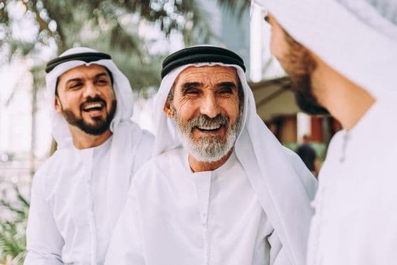 An elderly Emirati man conversing with two younger individuals.