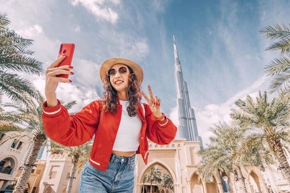 Young woman, in a red top, taking a selfie with the Burj Khalifa in the background.