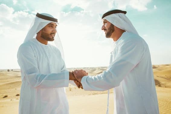 Two Arab men shaking hands in the desert.