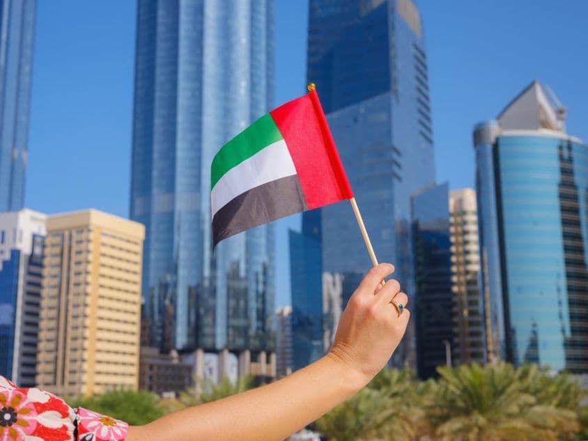 Woman's hand holding UAE flag with skyscrapers in the background.