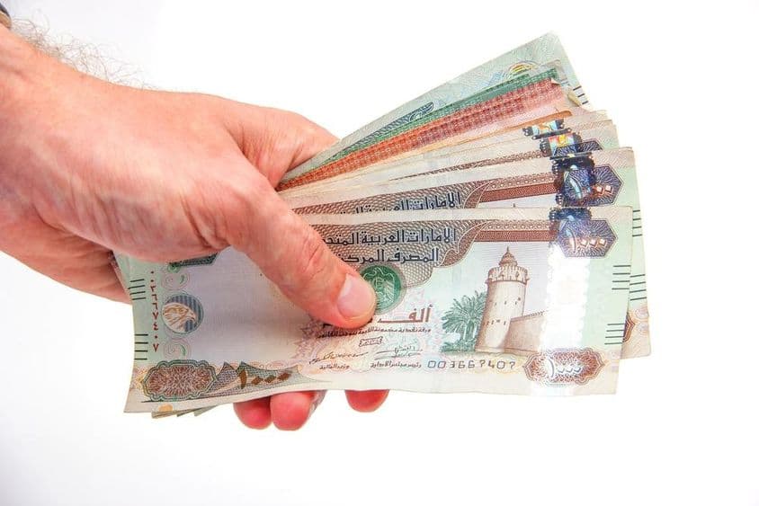 A man's hand holding dirhams.