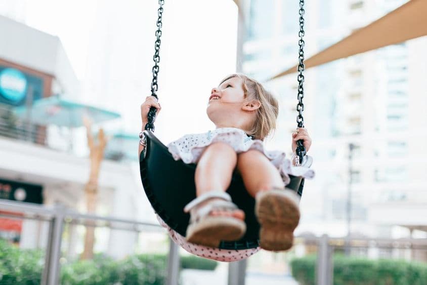 Happy little girl swinging in the kindergarten yard.