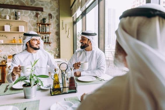Three businessmen drinking tea in Dubai, wearing traditional Emirati attire.