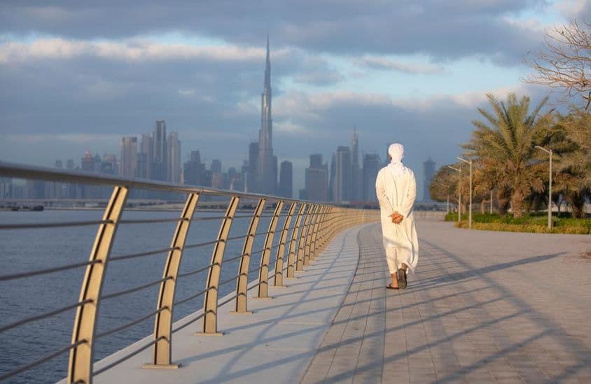 Emirati man walking on a sidewalk with Burj Khalifa in the background.