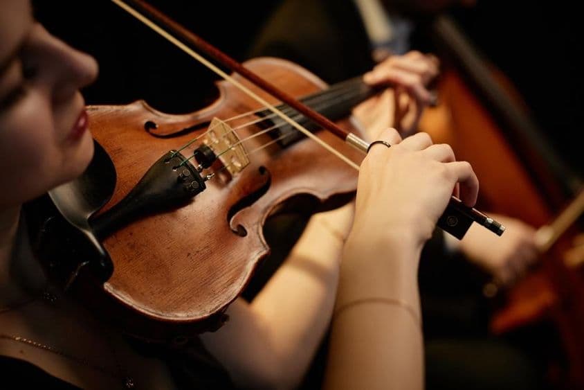 Female orchestra musician playing the violin with a bow during a concert on stage.