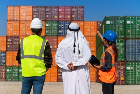 Middle Eastern businessman and engineers working outside a large commercial dock.