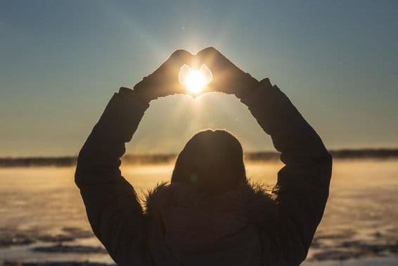 Woman forming hearts with her hands outdoors in a frosty sunset.