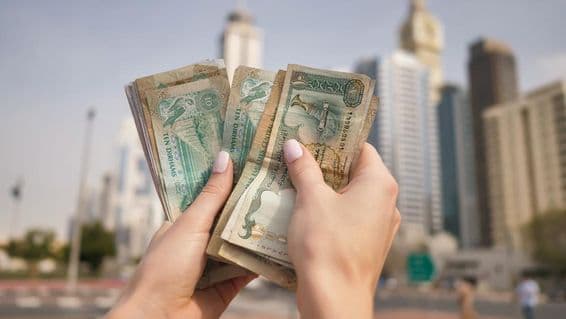 A girl holding UAE currency with Dubai skyscrapers in the background.