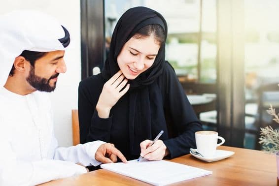 Arab man handing documents for signing to a woman wearing a hijab.