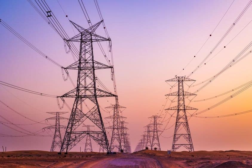 High voltage tower with power transmission lines against colorful sky in Al Qudra desert, Dubai, United Arab Emirates.