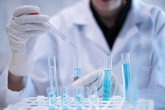 Scientist pipetting blue liquid into a test tube in a laboratory.
