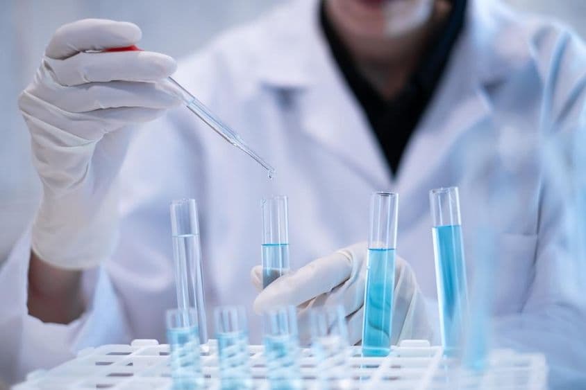 Scientist pipetting blue liquid into a test tube in a laboratory.
