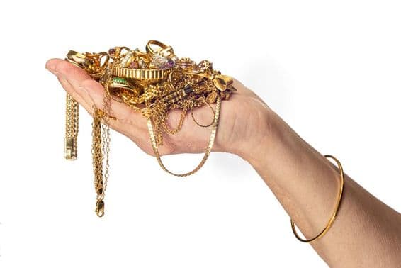 A woman's hand holding a pile of gold jewelry and wearing a bracelet.
