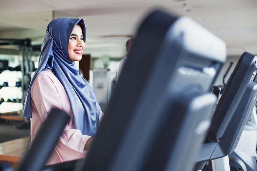 Muslim woman exercises in a gym, wearing a hijab.