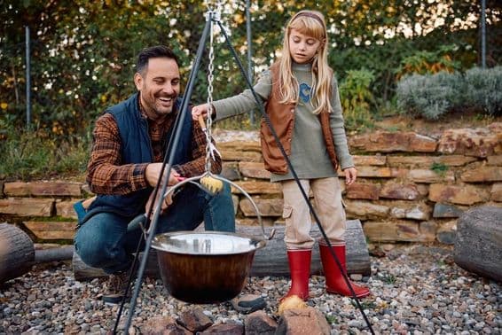 Little girl helps her father cook over a campfire in the wild during autumn.