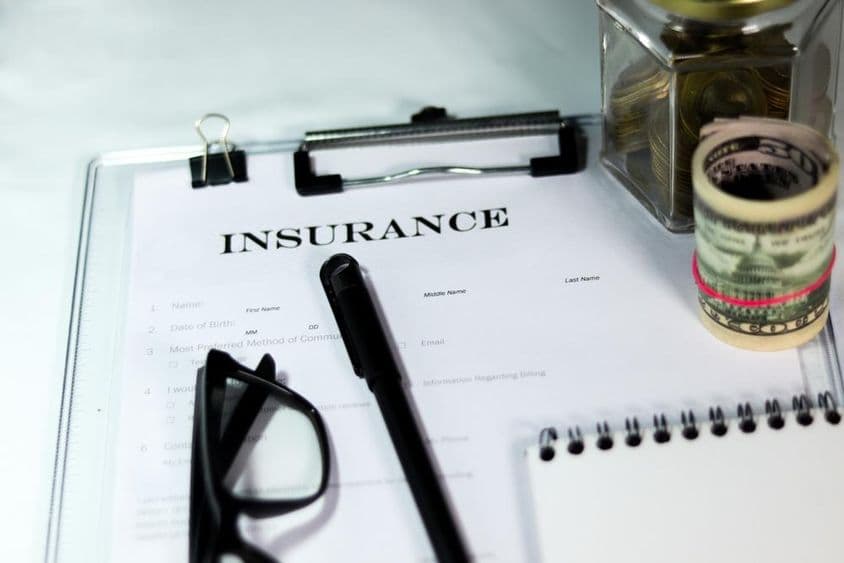 Insurance form with coin box, dollar bundle, pen, and glasses.