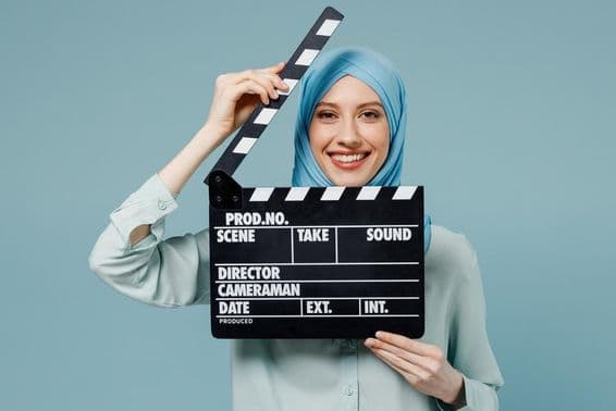 Young Arab Muslim woman in abaya hijab holding a classic black film clapper.