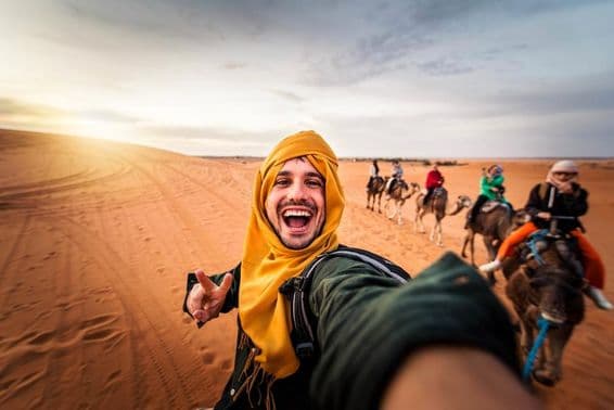 Happy tourist enjoying camel riding in the desert.