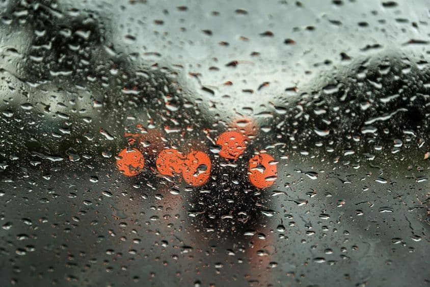 Rainy day in Dubai with visible car lights in the distance, seen through a car window with rain droplets.