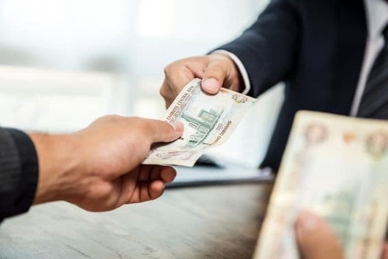 Businessman handing money in UAE dirham currency to a partner.