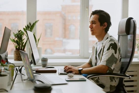Young programmer sitting at a desk, coding on a computer in a bright office.