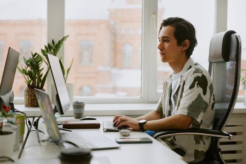 Young programmer sitting at a desk, coding on a computer in a bright office.
