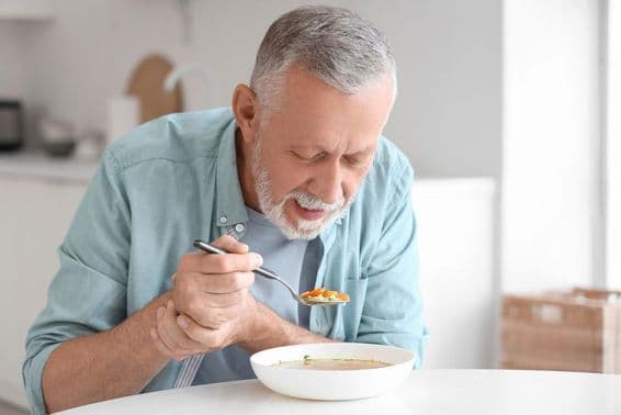 Elderly man with Parkinson's eating at a kitchen table.