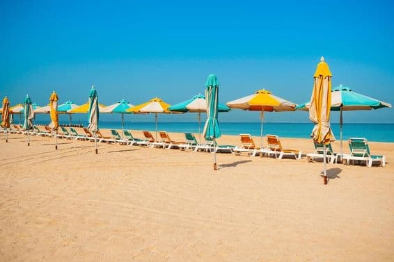 Dubai public beach, sandy shore, sun loungers, and blue sea.