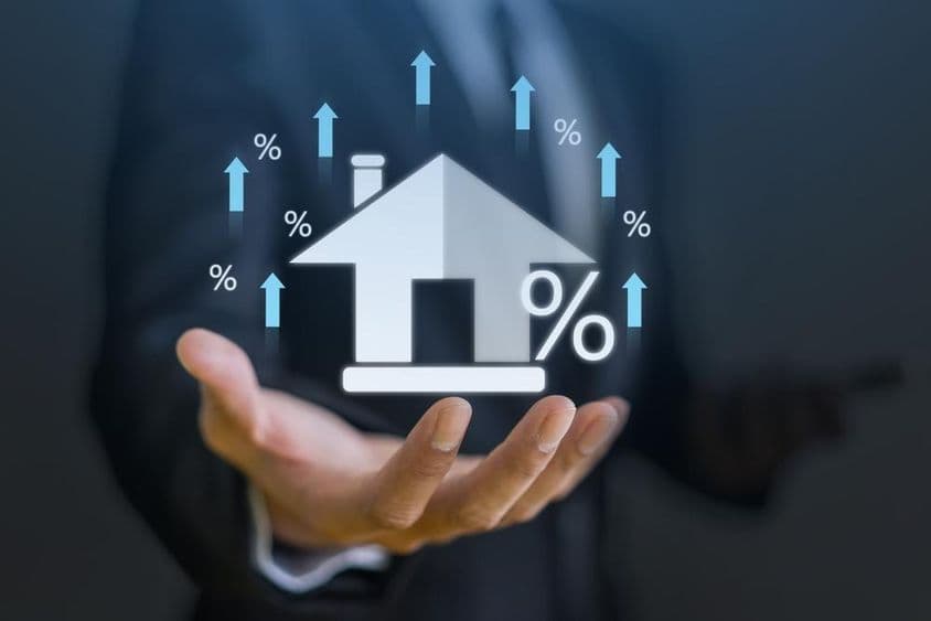 Businessman holding a hologram of a house with an upward index indicator.
