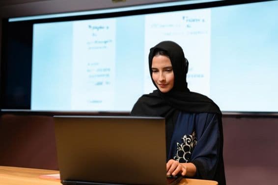 Female teacher wearing Abaya Hijab with projector screen background in a modern classroom with digital screen.