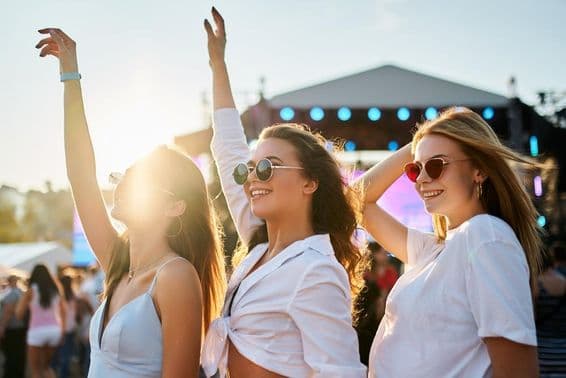Girls in summer dresses enjoying a concert, celebrating with raised hands.