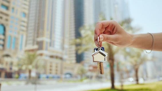 Woman's hand holding apartment key, skyscrapers in background.