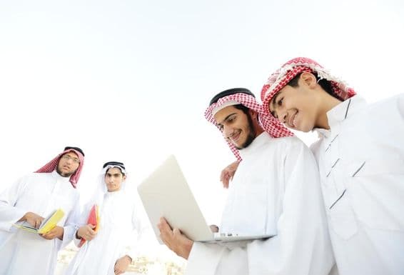 Happy Arab students viewing educational content on a laptop.