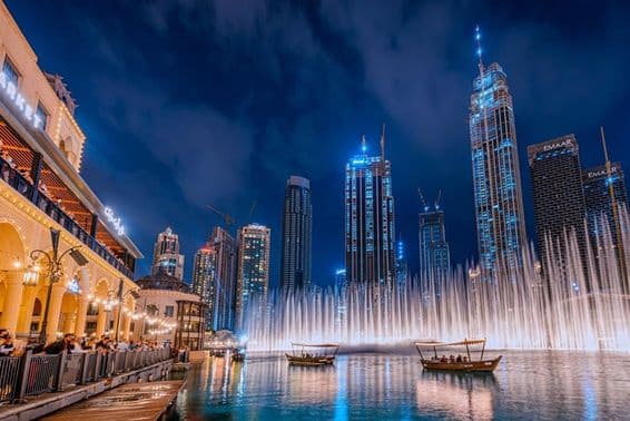 People boating while watching the Dubai fountain show at night, with Dubai skyscrapers in the background.