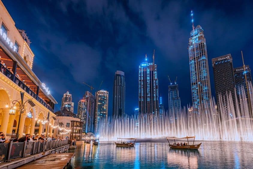 People boating while watching the Dubai fountain show at night, with Dubai skyscrapers in the background.