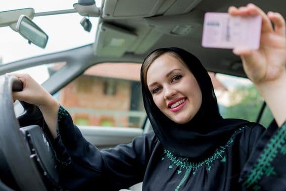 Muslim woman driving a car, holding a license.