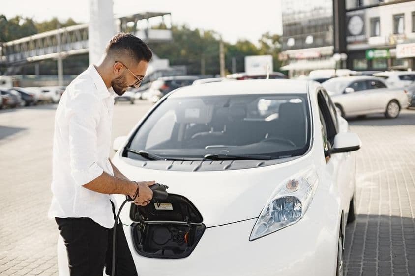 Young Arab man charging a white electric car.