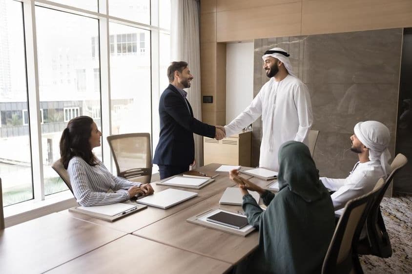 Arab and European businesspeople shake hands at a team meeting, corporate discussion.