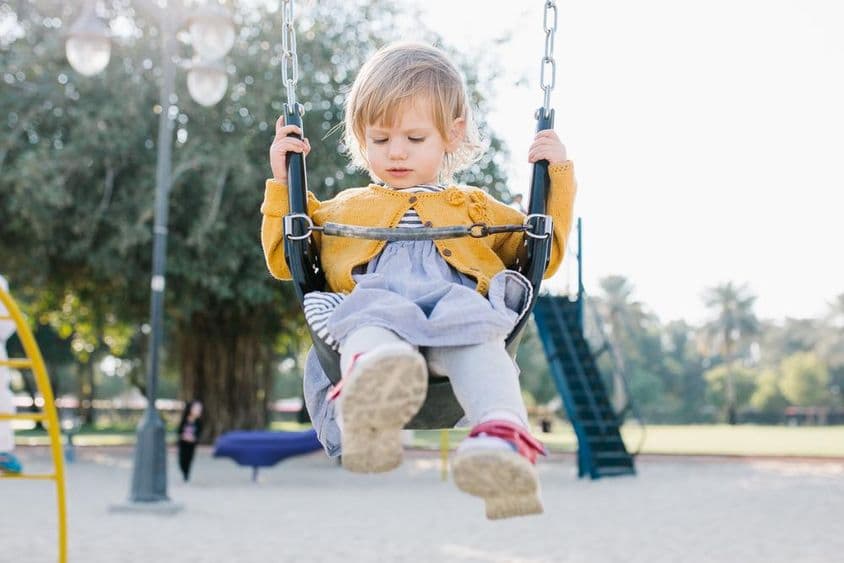 Happy toddler girl swinging in the park in sunshine.