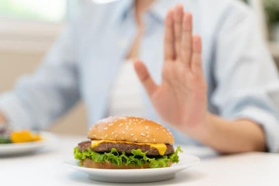 A woman refuses a fast-food hamburger high in fat.