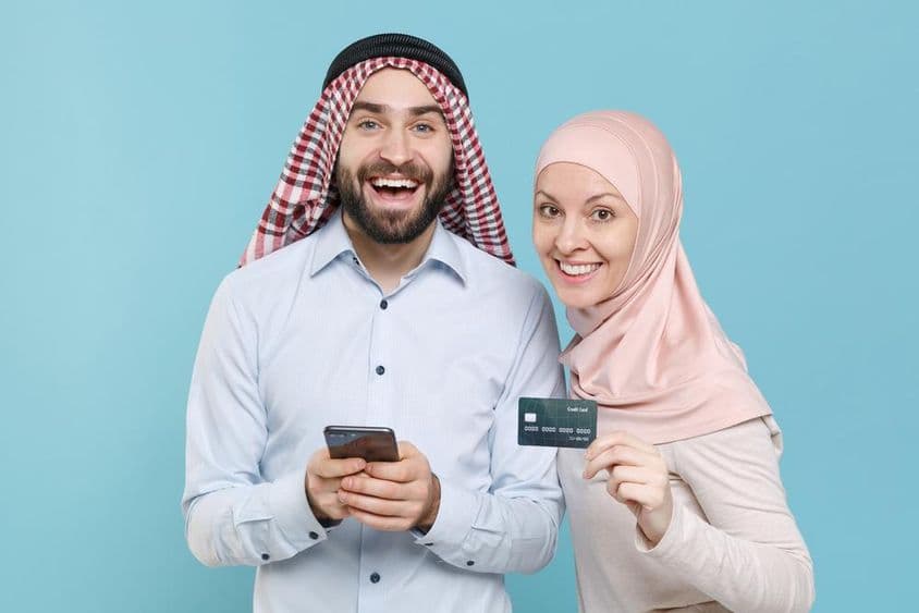 Smiling couple holding credit card and phone.
