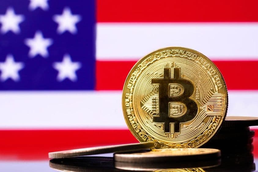 Gold Bitcoin metal coin with the USA flag in the background.