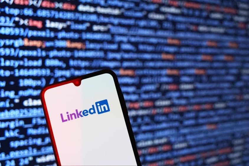 Smartphone displaying LinkedIn logo with code snippet in the background.