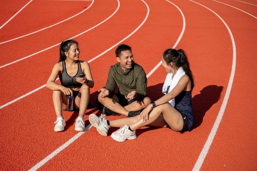 A group of cheerful athletes resting on a sports field under the sun after training.