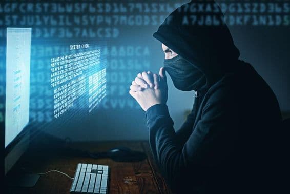 Cybercrime, hooded man sitting in front of a computer.