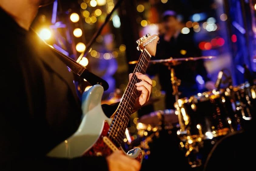 A guitarist playing a chord on the fretboard during a band's performance.